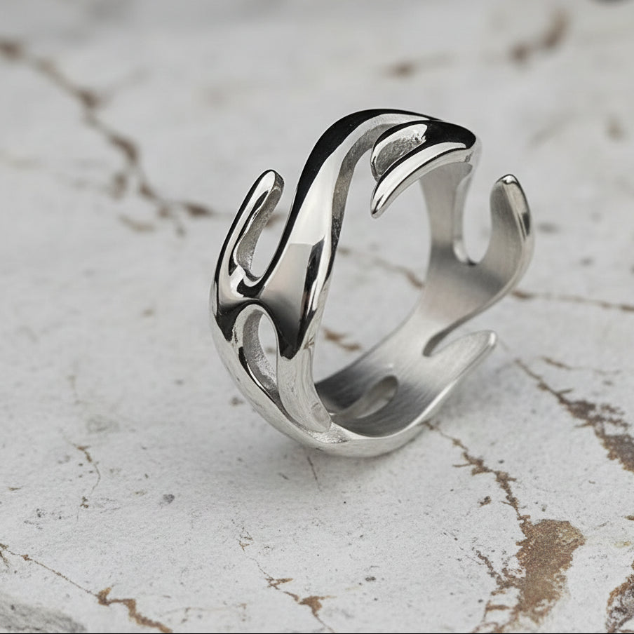 Ein versilberter Edelstahlring mit Flammenmotiv, präsentiert auf einer dunklen strukturierten Oberfläche.