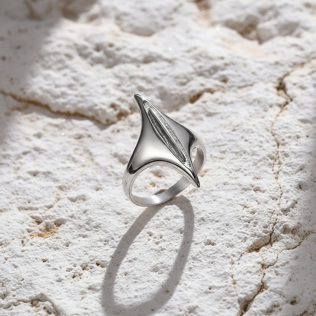Ein versilberter Edelstahlring mit geometrischem Design, präsentiert auf einer strukturierten grauen Oberfläche.
