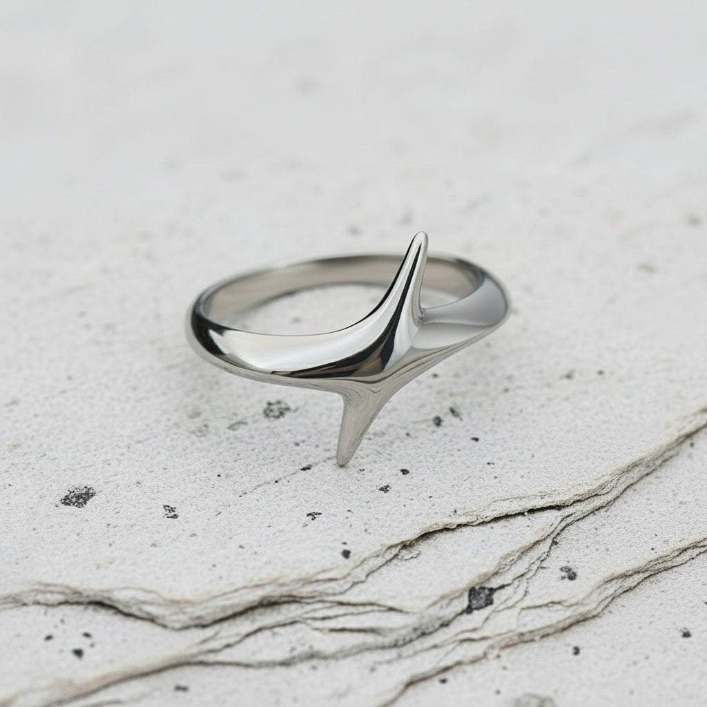 Ein versilberter Edelstahlring mit schrägem Design, auf einer Holzoberfläche platziert.